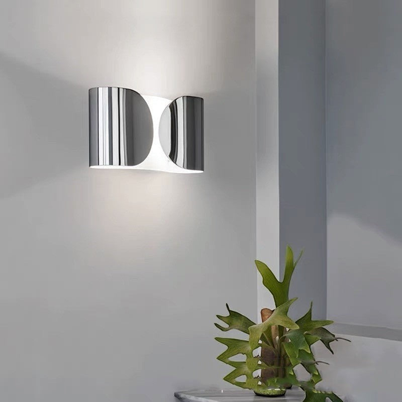 Applique murale design moderne Lumeoo en métal chromé brillant diffusant une lumière douce sur un mur gris