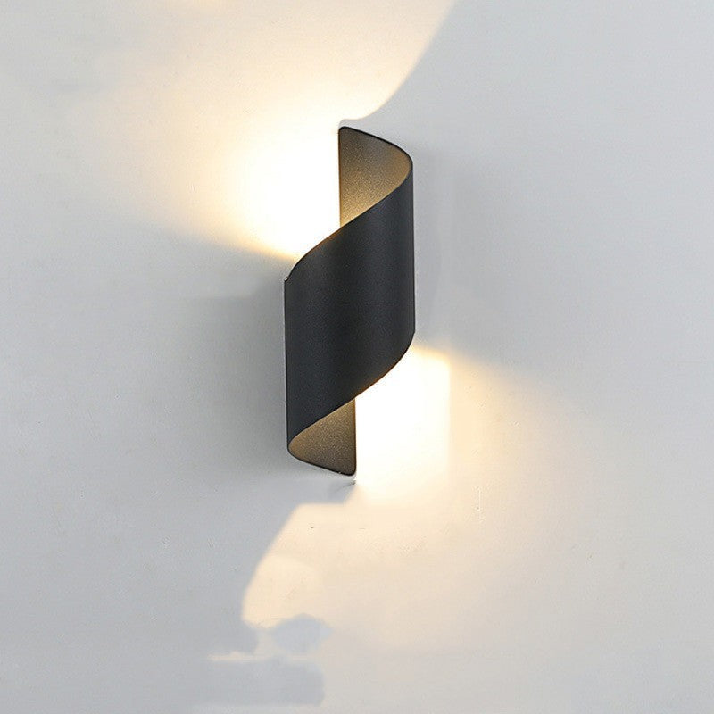 Applique murale extérieure LED Lumeoo noire au design incurvé moderne diffusant une lumière douce sur un mur blanc