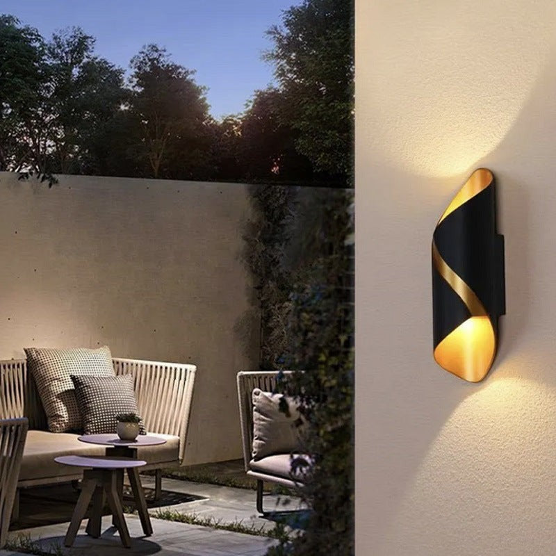 Applique murale extérieure Lumeoo WALLEX noire et dorée au design torsadé moderne sur une terrasse éclairée