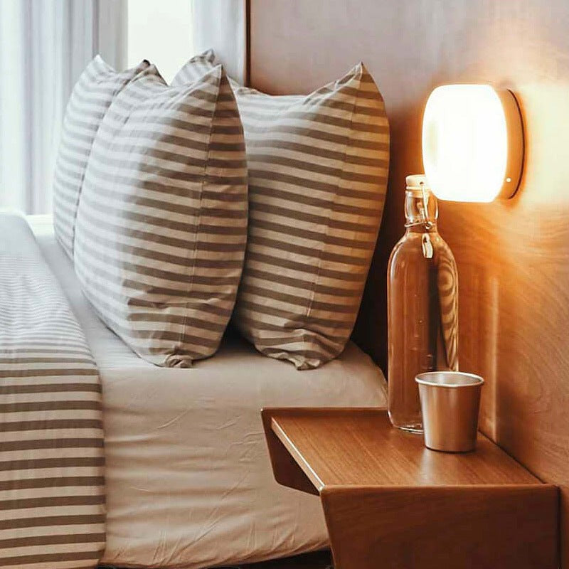Applique murale LED ronde Lumeoo diffusant une lumière douce et chaleureuse au-dessus d'une table de chevet en bois