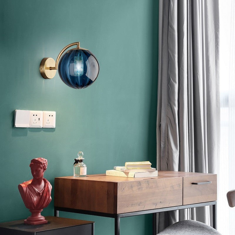 Applique murale Lumeoo GLOBWAX en verre bleu en forme de boule avec support en métal doré dans une chambre élégante