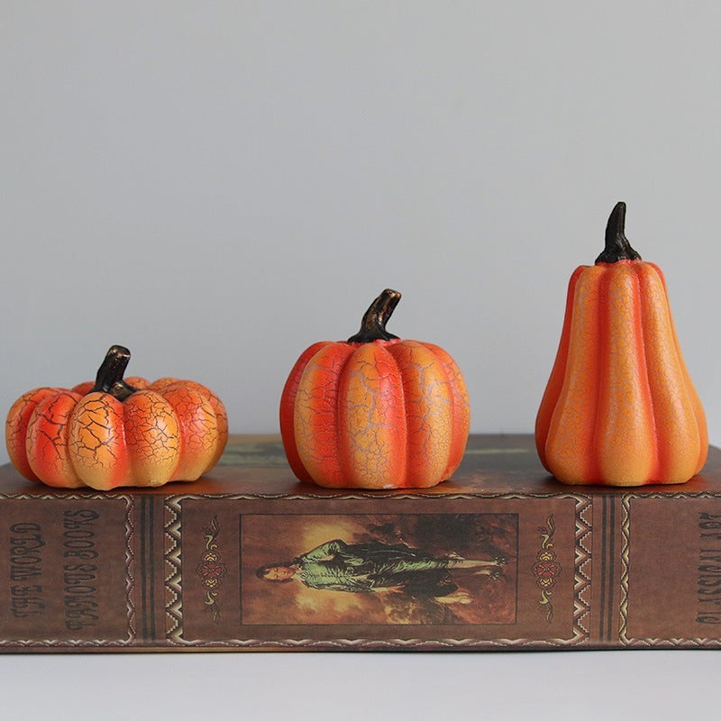 Trois citrouilles décoratives Lumeoo en résine orange avec effet craquelé, posées sur un livre ancien.