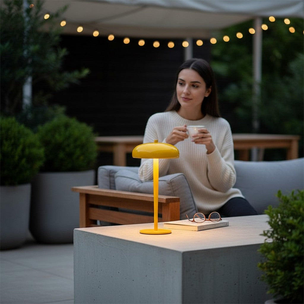 Lampe champignon Lumeoo jaune rechargeable sur une table de terrasse avec une femme en arrière-plan