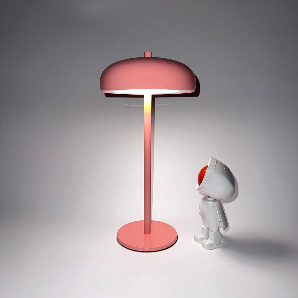 Lampe champignon rose minimaliste rechargeable Lumeoo avec éclairage doux posée à côté d'une figurine décorative
