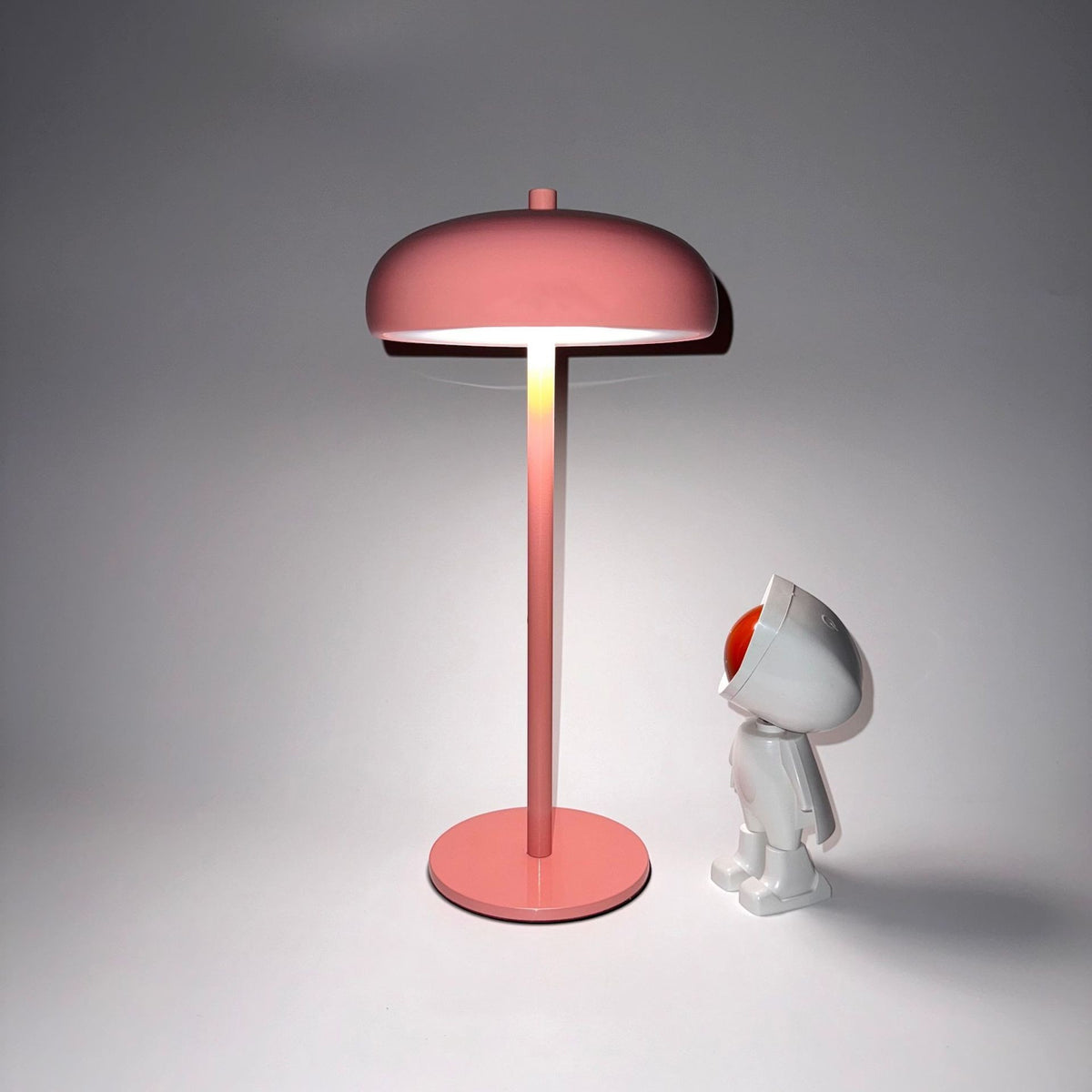 Lampe champignon rose minimaliste rechargeable Lumeoo avec éclairage doux posée à côté d'une figurine décorative