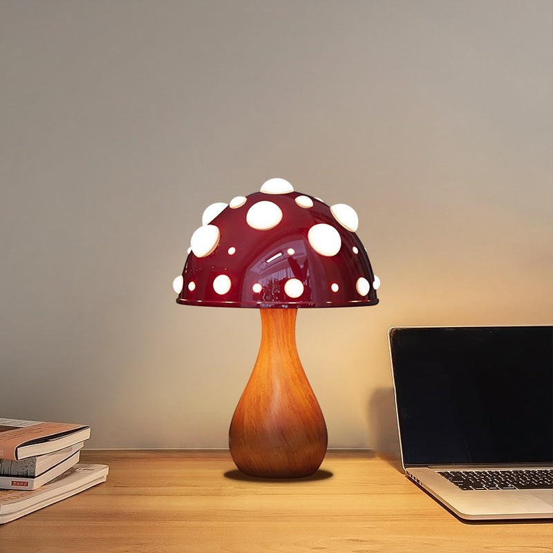 Lampe champignon Lumeoo rouge à pois blancs avec pied en bois sur un bureau près d'un ordinateur portable