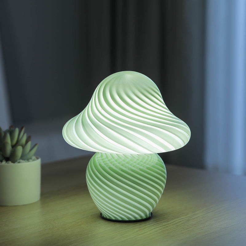 Lampe champignon Lumeoo en pâte de verre vert clair avec motif torsadé diffusant une lumière douce sur une table
