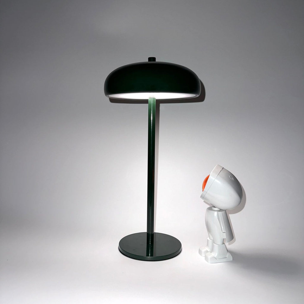 Lampe champignon Lumeoo vert foncé minimaliste et rechargeable posée sur une table à côté d'une figurine robot