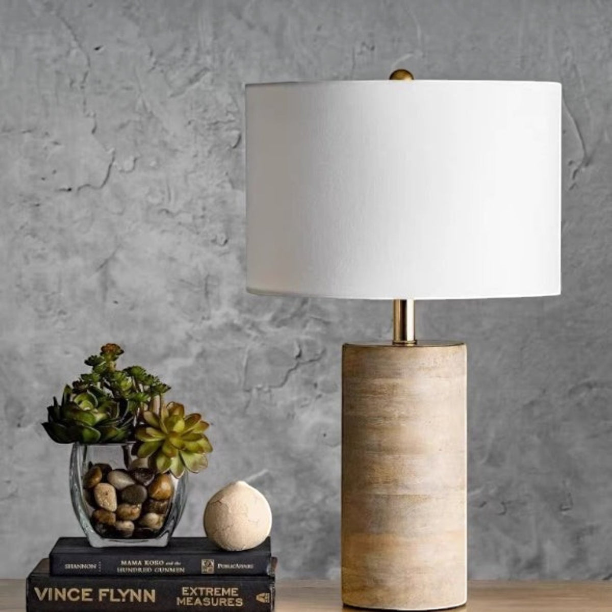 Lampe de chevet Lumeoo avec pied cylindrique en bois naturel et abat-jour blanc, posée sur des livres près de plantes.
