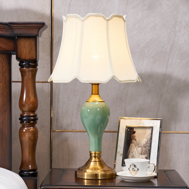 Lampe de chevet Lumeoo en céramique vert sauge avec abat-jour festonné crème et base en laiton doré sur table de nuit