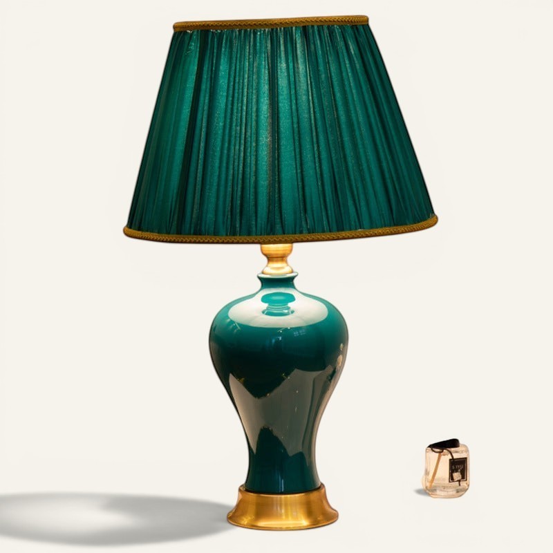 Lampe de chevet Lumeoo style européen avec abat-jour plissé vert émeraude, pied en céramique brillante et base dorée.