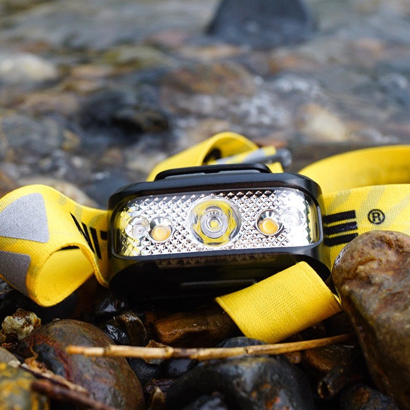 Lampe frontale Lumeoo TRAILUX rechargeable avec bandeau jaune réfléchissant posée sur des rochers au bord de l'eau.