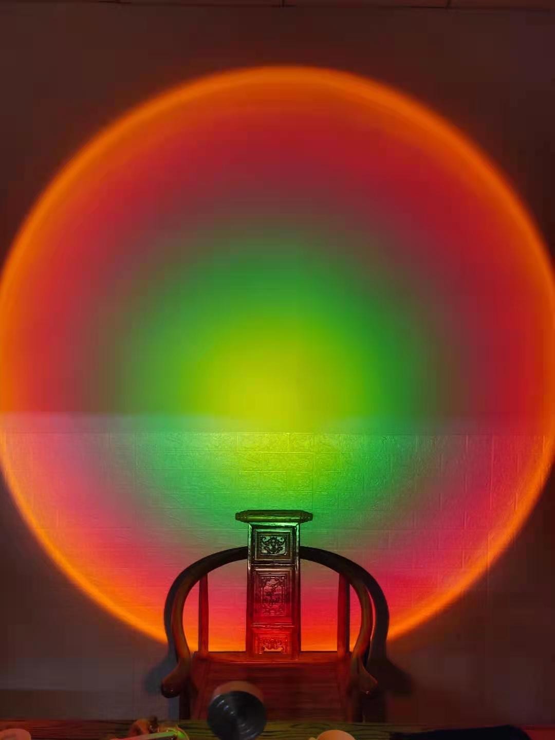 Lampe Lumeoo projetant un halo lumineux aux couleurs dégradées de coucher de soleil sur un mur derrière une chaise en bois