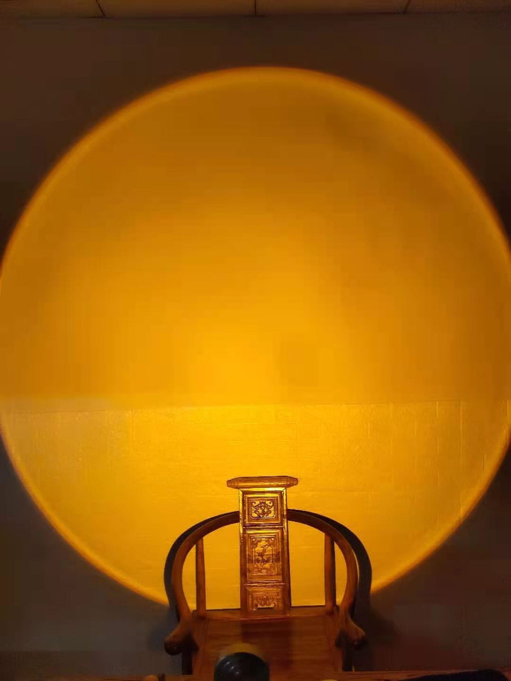 Lampe Lumeoo projetant un halo lumineux doré rappelant un coucher de soleil sur un mur au-dessus d'une chaise en bois
