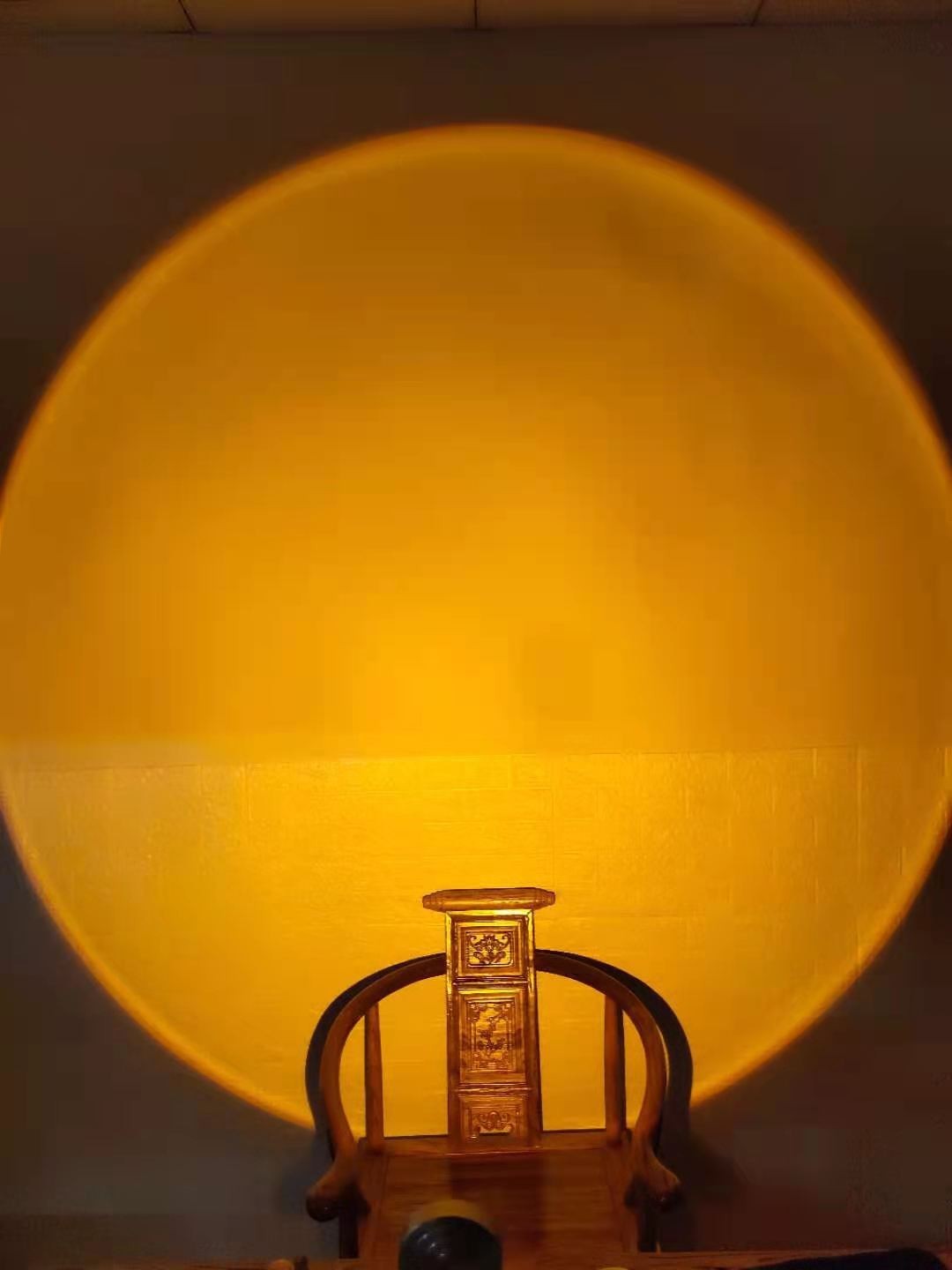 Lampe Lumeoo projetant un halo lumineux doré rappelant un coucher de soleil sur un mur au-dessus d'une chaise en bois