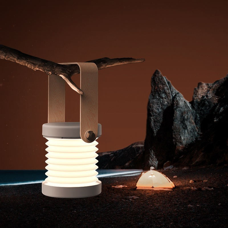 Lanterne LED pliable Lumeoo, tactile et rechargeable, suspendue à une branche dans un décor de camping nocturne.