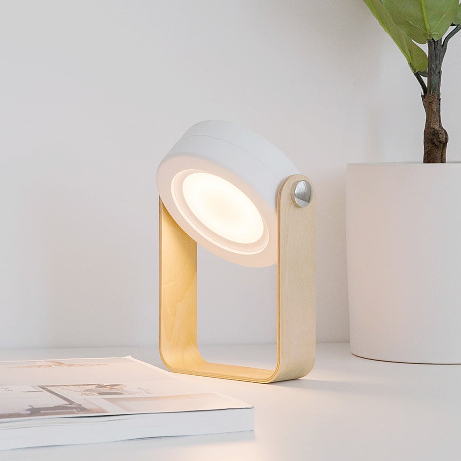 Lanterne LED Lumeoo pliable et tactile, design blanc et bois clair, diffusant une lumière chaude sur un bureau.