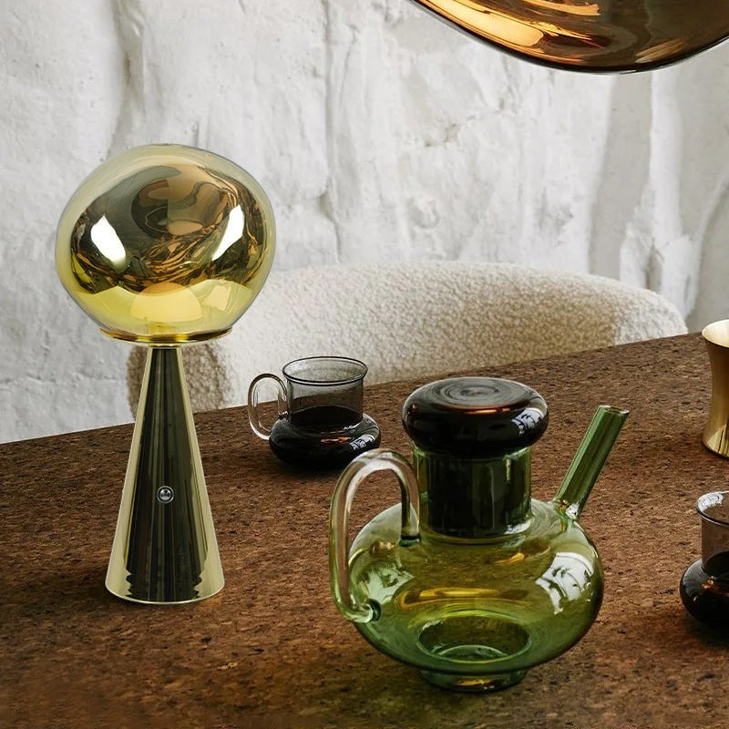 Lampe à lave Lumeoo rechargeable dorée au design minimaliste et moderne posée sur une table en liège.