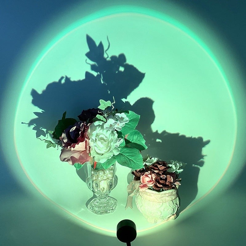 Lampe Lumeoo RAINOVA projetant un cercle lumineux vert sur un mur avec des fleurs en premier plan