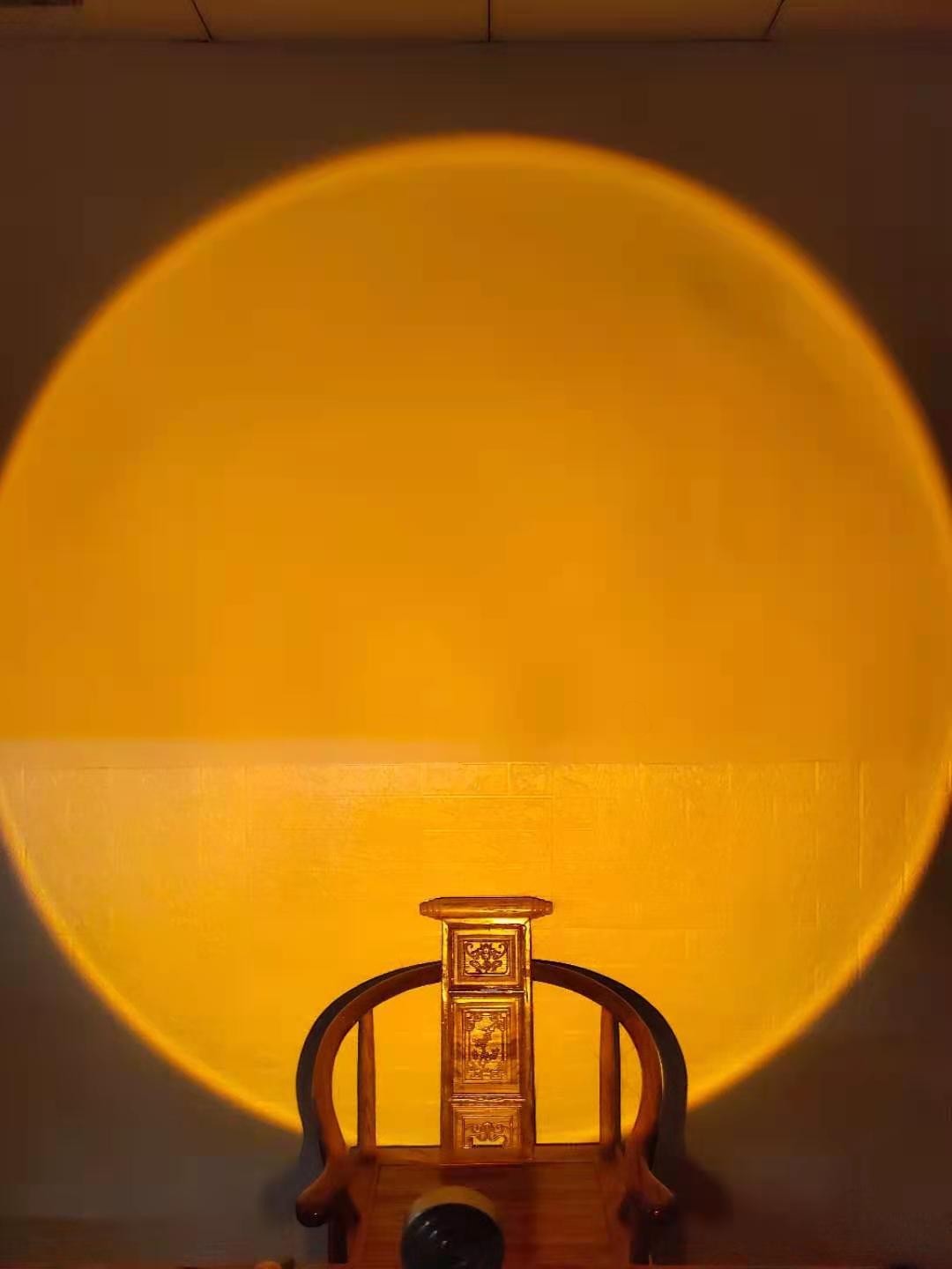 Lampe Lumeoo projetant un cercle lumineux doré rappelant un coucher de soleil sur un mur au-dessus d'une chaise en bois