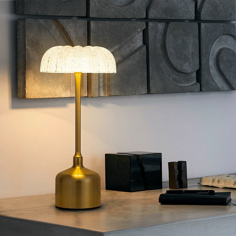 Lampe de table Lumeoo IRONOVA dorée avec abat-jour en verre texturé diffusant une lumière douce sur une console.