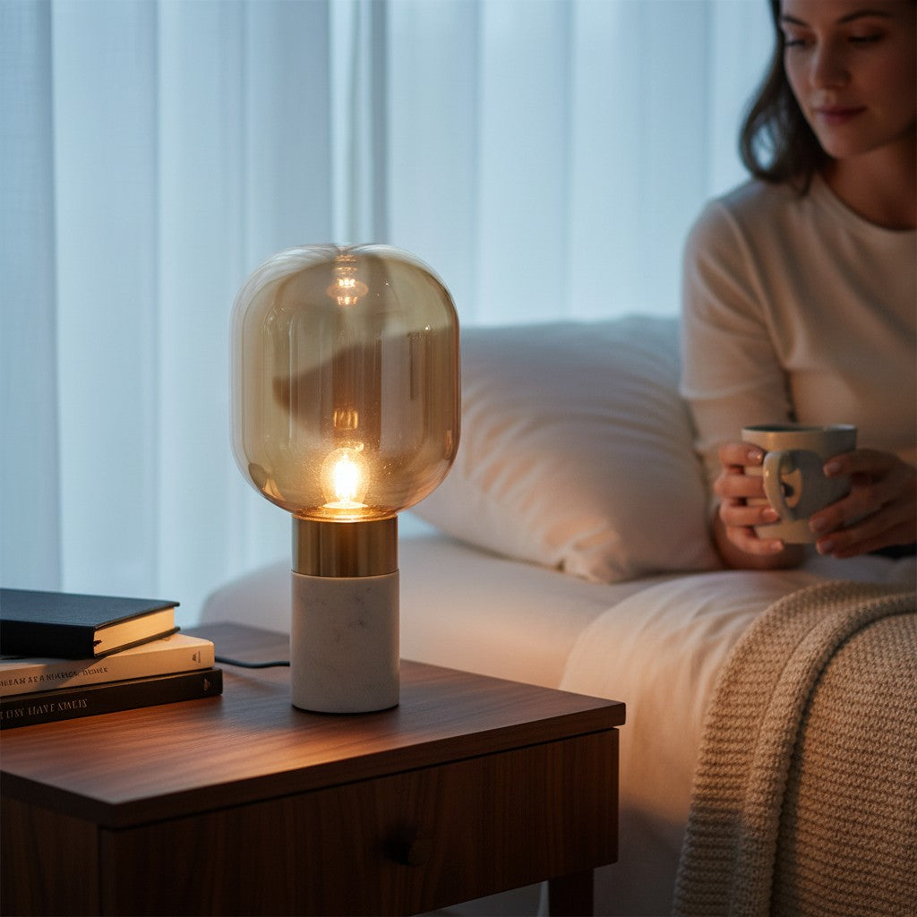 Lampe de table design Lumeoo avec globe en verre ambré, base en marbre blanc et détails dorés sur une table de nuit Image