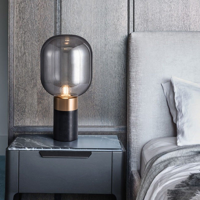 Lampe de table design Lumeoo avec globe en verre fumé, base en marbre noir et détails en métal doré sur une table de nuit