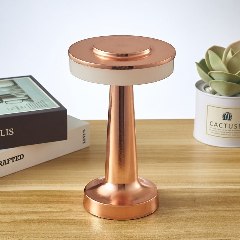 Lampe de table sans fil Lumeoo dorée au design minimaliste posée sur une table en bois avec des livres et une plante