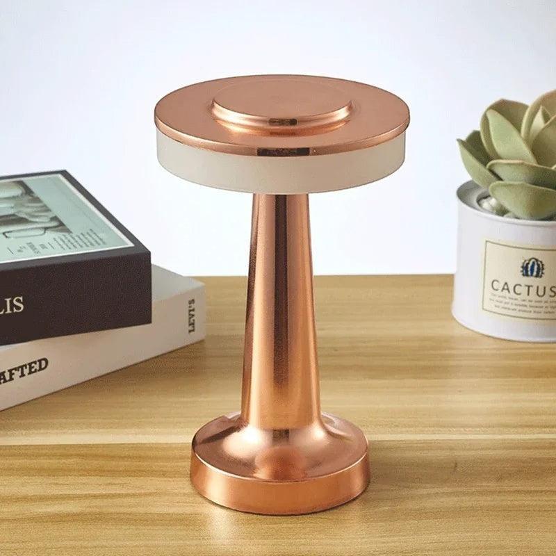 Lampe de table sans fil Lumeoo au design doré élégant posée sur un bureau en bois avec des livres et une plante