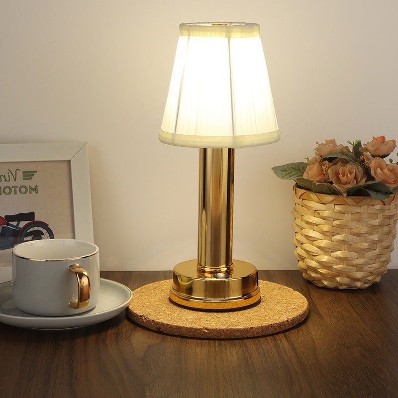 Lampe de table LED rechargeable Lumeoo dorée avec abat-jour plissé blanc sur un sous-verre en liège