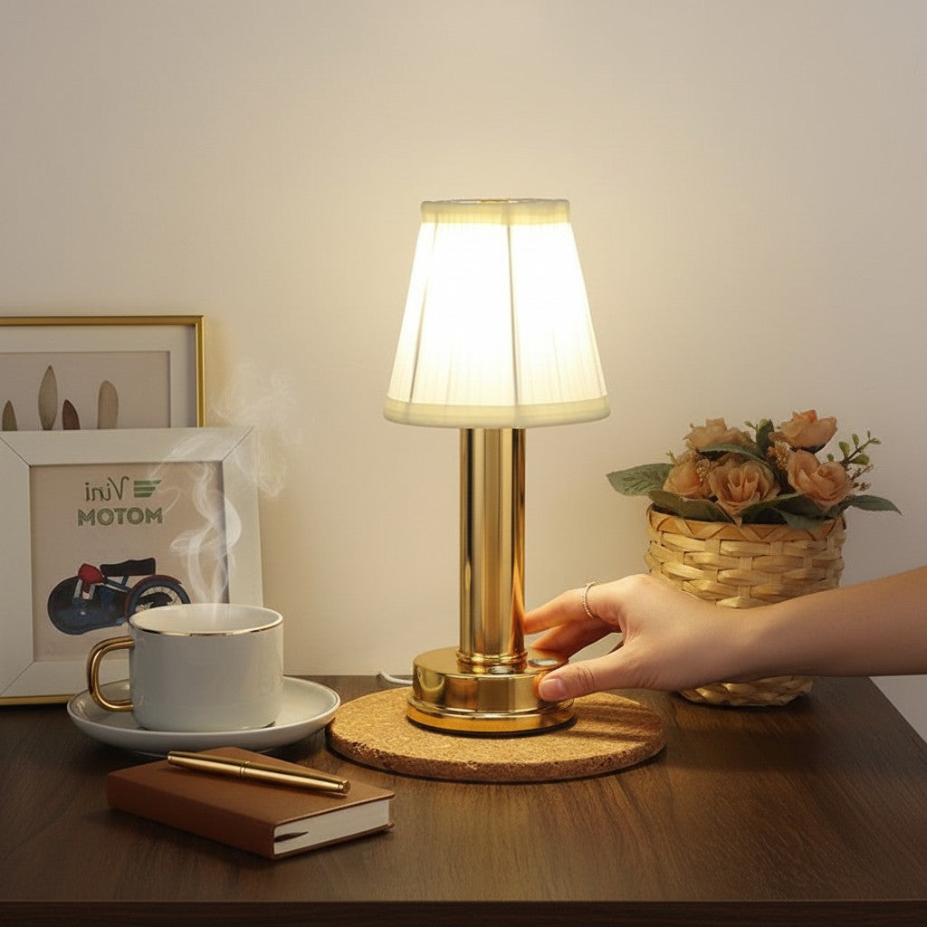 Lampe de table LED rechargeable Lumeoo dorée avec abat-jour en tissu sur une table en bois avec tasse de café