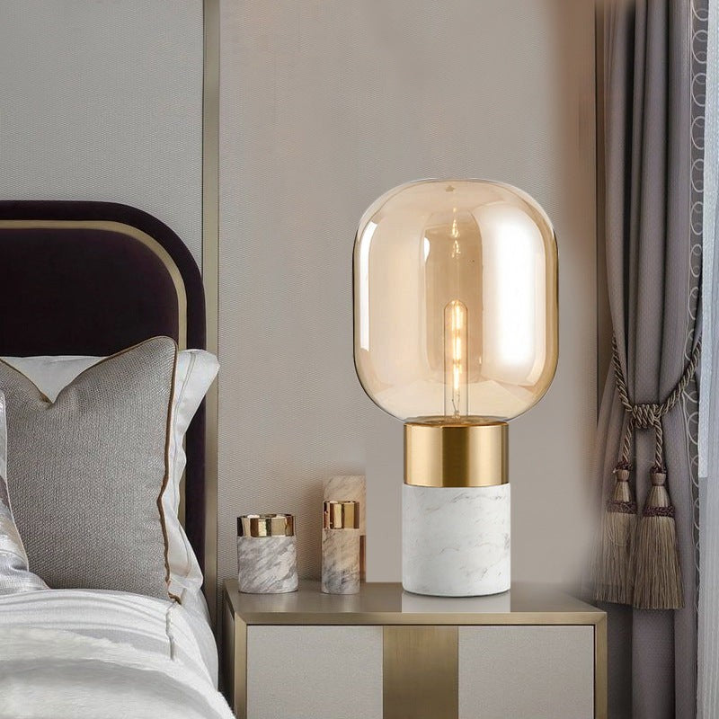 Lampe de table design Lumeoo avec globe en verre ambré, base en marbre blanc et détails dorés sur une table de chevet
