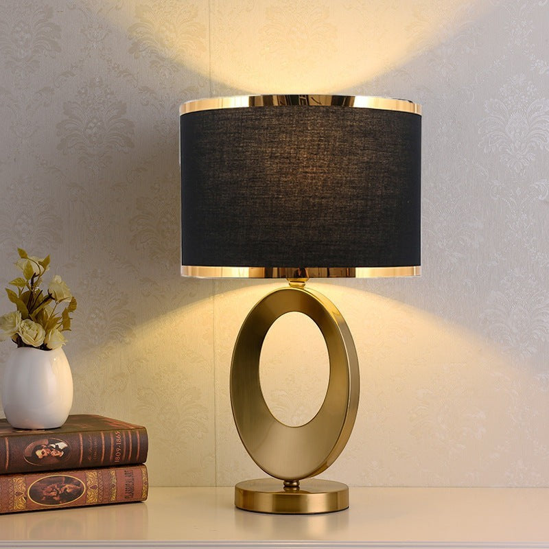 Lampe de table Lumeoo Orbilux avec base ovale dorée en métal et abat-jour cylindrique noir pour salon ou chevet