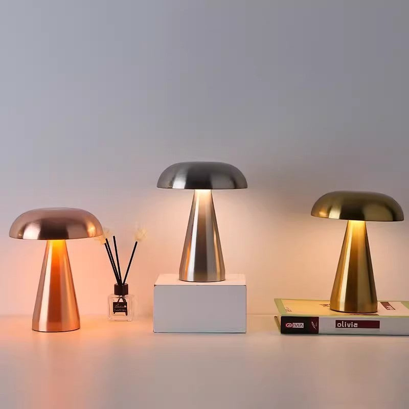 Trois lampes de table rechargeables Lumeoo au design rétro champignon en métal doré, argenté et cuivré sur une table