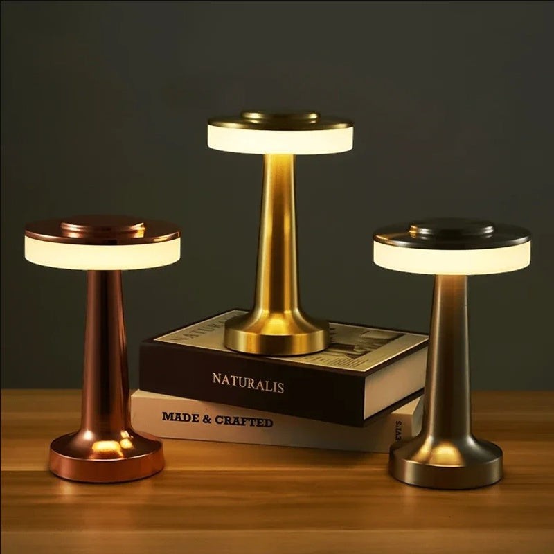 Trois lampes de table sans fil Lumeoo en finitions dorée, cuivrée et argentée posées sur des livres pour une ambiance chic