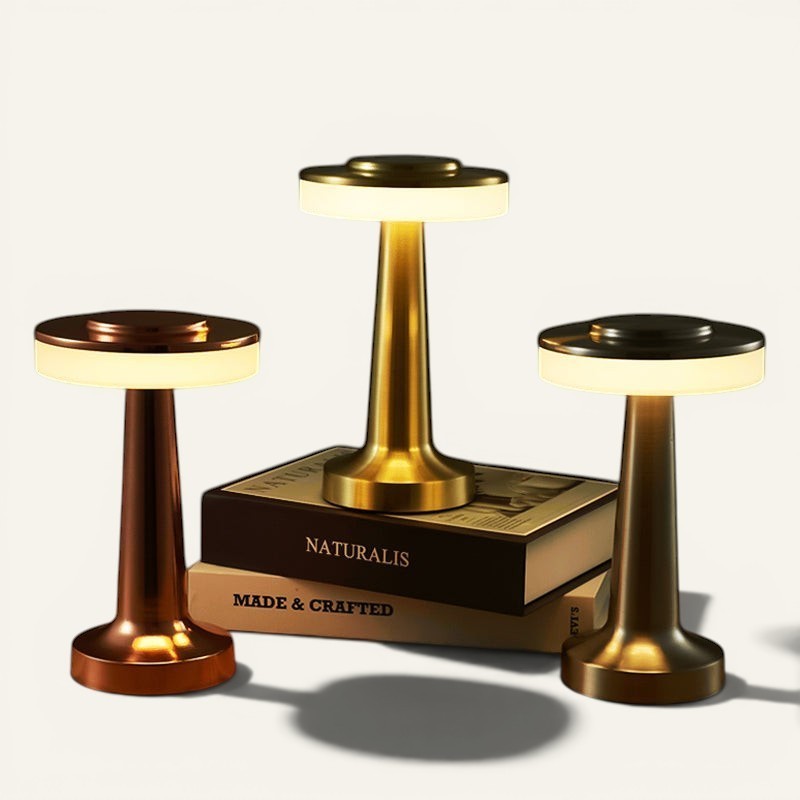 Trois lampes de table sans fil Lumeoo en métal doré, cuivré et bronze, design LED tactile et dimmable sur des livres