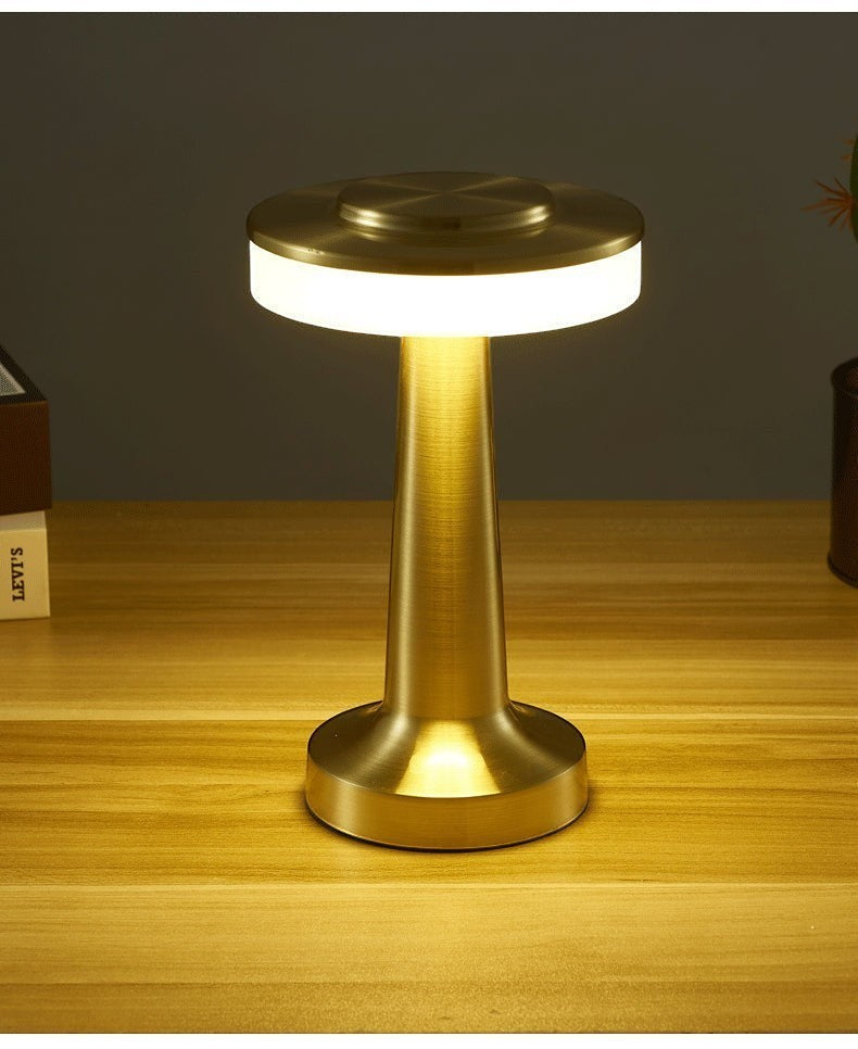 Lampe de table sans fil Lumeoo en métal doré, design tactile LED rechargeable et dimmable sur un bureau en bois.