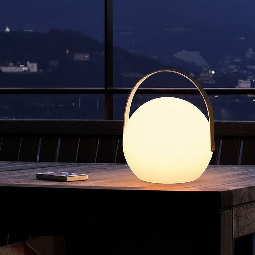 Lanterne Lumeoo GLAMPA LED rechargeable, sphérique avec anse, 16 couleurs et télécommande sur une table de terrasse.