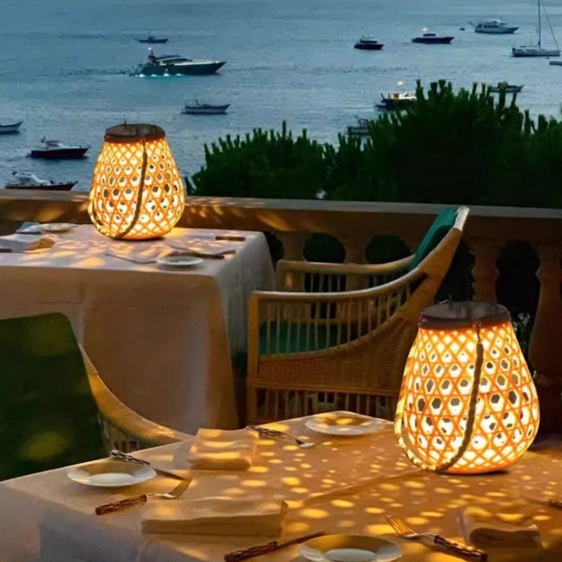 Lanterne solaire Lumeoo style rotin posée sur une table de terrasse avec vue sur la mer au coucher du soleil