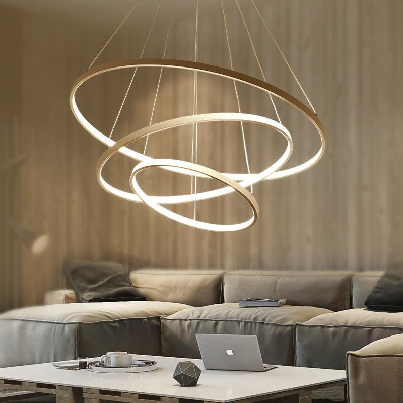 Lustre LED Lumeoo à trois anneaux dorés suspendus au-dessus d'un salon moderne pour un éclairage design et chaleureux