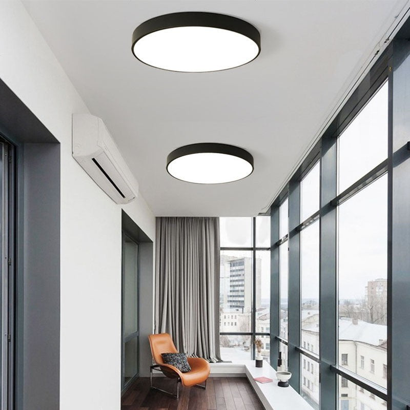 Plafonnier LED Lumeoo rond ultra-plat noir avec éclairage diffus dans un salon moderne avec vue panoramique