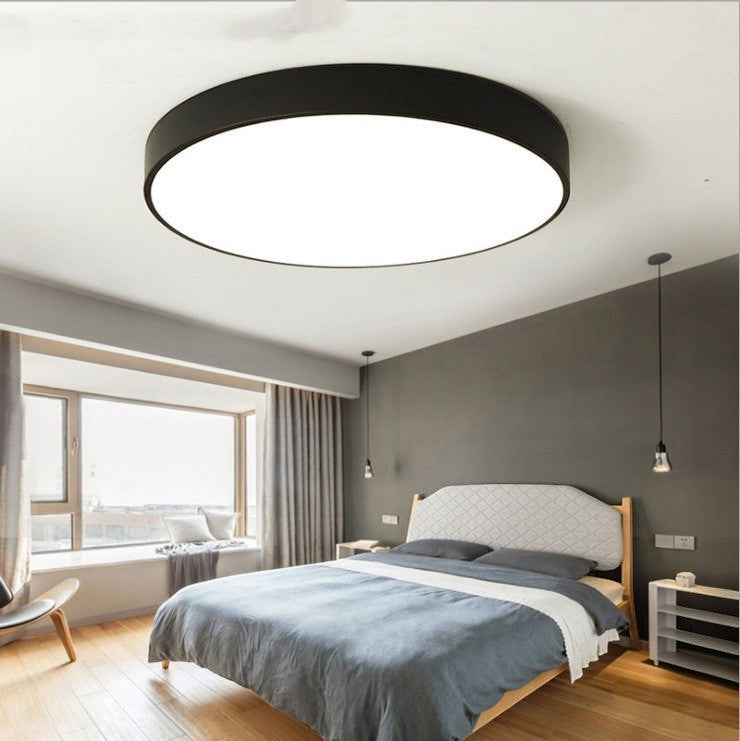 Plafonnier LED rond ultra-fin noir Lumeoo installé au plafond d'une chambre moderne à la décoration minimaliste