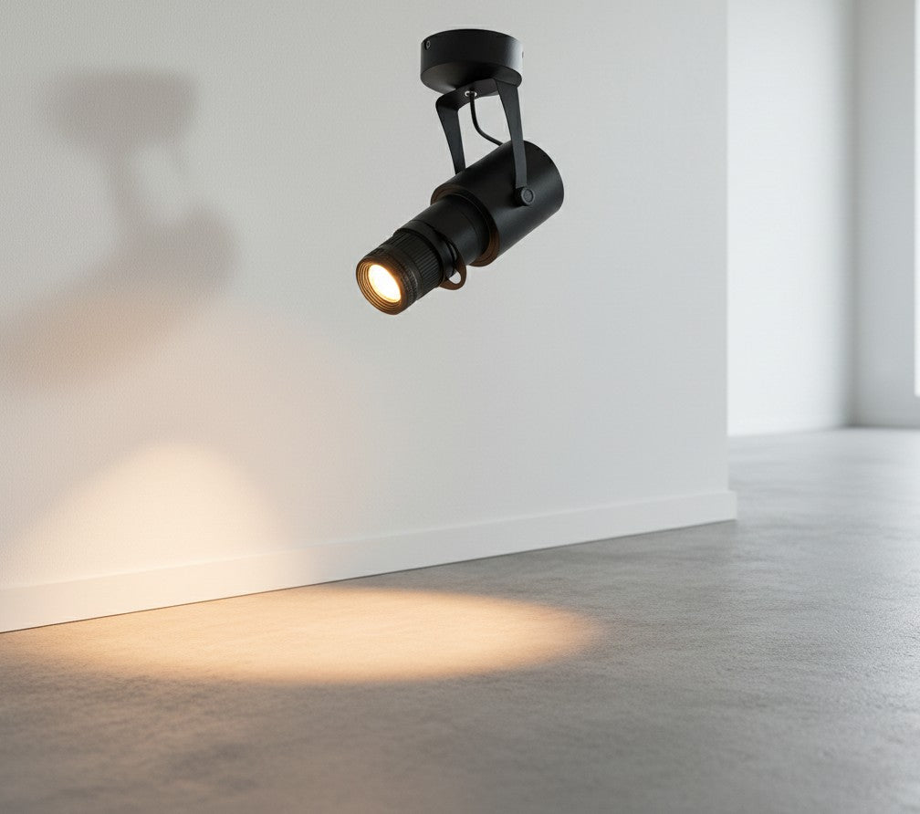 Spot LED orientable Lumeoo noir au design moderne projetant un faisceau lumineux chaud sur un mur blanc