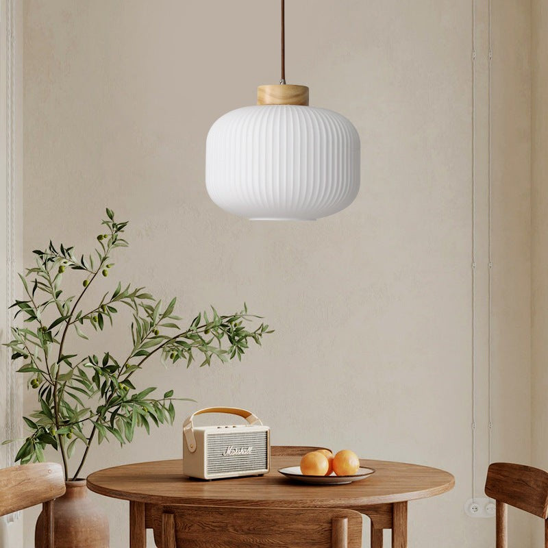 Suspension Lumeoo en bois et verre blanc strié au design rétro, installée au-dessus d'une table en bois dans une chambre