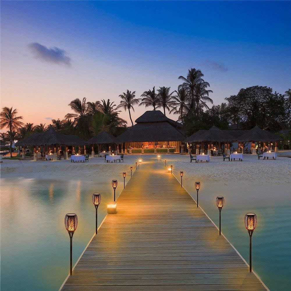 Torche solaire LED Lumeoo décorative pour jardin, diffusant une lumière chaleureuse le long d'un ponton en bois au crépuscule.